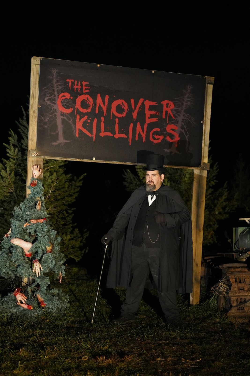A figure in a top hat beside The Conover Killings sign, a wreath of severed limbs overhead